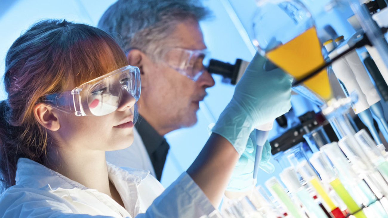 Attractive young female scientist and her senior male supervisor pipetting and microscoping in the life science research laboratory (biochemistry, genetics, forensics, microbiology..)